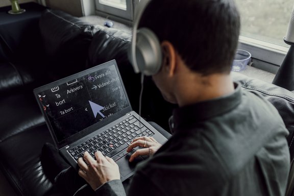 Person mit Kopfhörern sitzt auf Sofa und bedient Laptop mit großer Bildschirmlupe