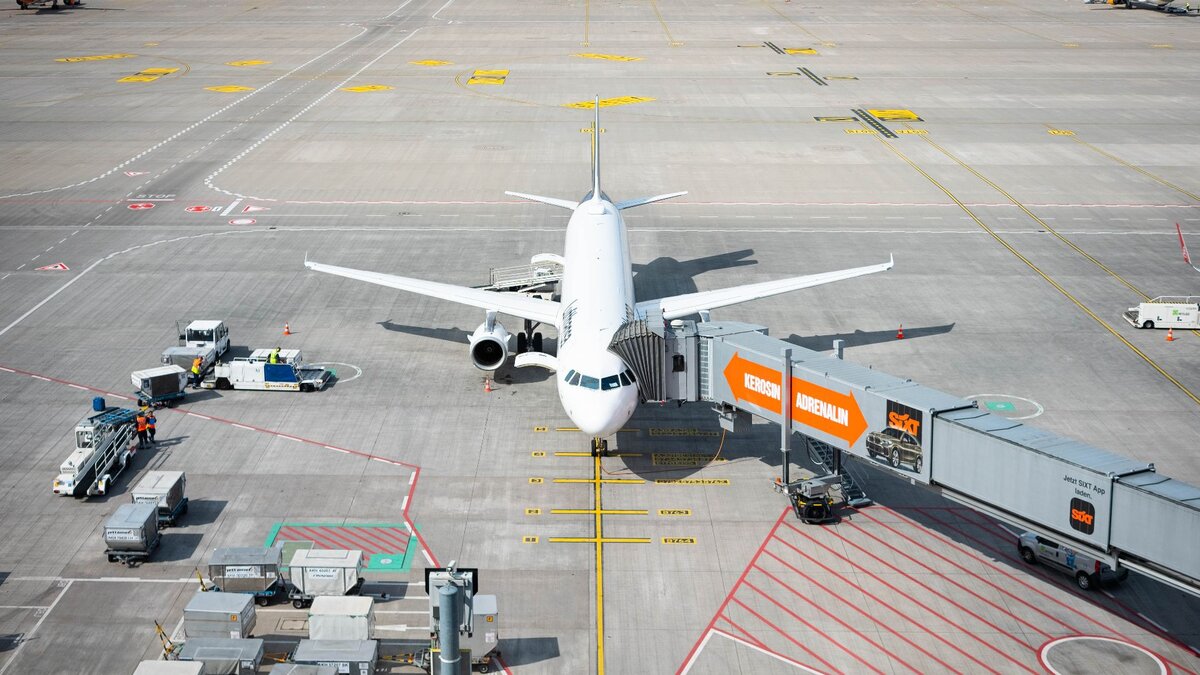 Zu sehen ist ein Passagierflugzeug, welches durch einen Gang mit dem Terminal verbunden ist, damit die Menschen zu- oder aussteigen können. Es handelt sich um eine Szene auf dem Flughafen BER in Berlin.