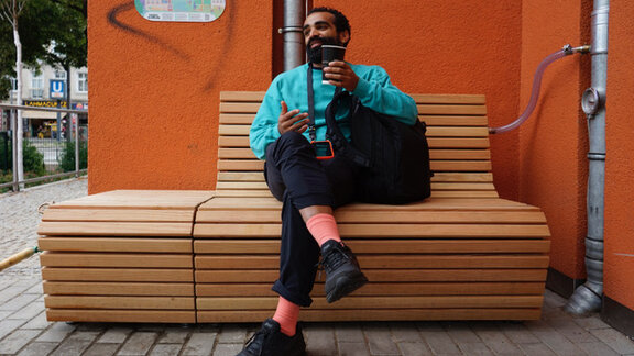 Ein Mann sitzt auf einer Regenwasserbank und telefoniert.  