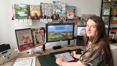 Marlene Käseberg sitzt an einem Schreibtisch mit drei Bildschirmen vor sich. Ihre Hände sind auf der Tastatur und auf der Maus
