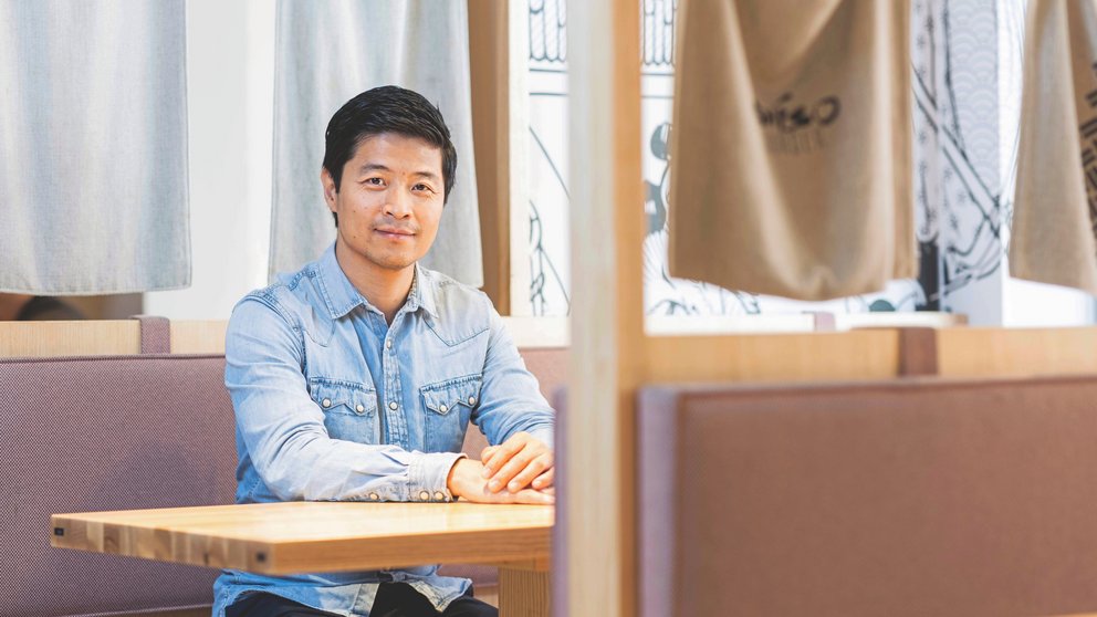 Ein asiatisch aussehender Mann sitzt an einem Tisch.