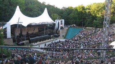 Zu sehen ist eine große Bühne, umgeben von Bäumen und einem großen Publikum. Es handelt sich um die Waldbühne in Berlin.