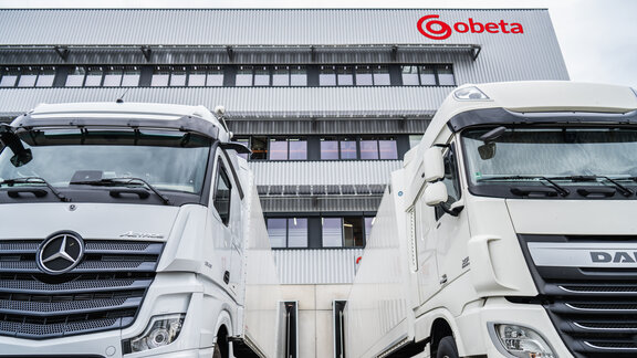 Zwei Weiße LKW stehen vor einem Bürogebäude mit der Aufschrift "Obeta"