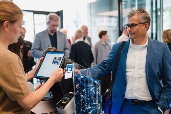 Zu sehen ist ein Mann, der an einem Eingang zu einer Art messe ein Ticket erhält.