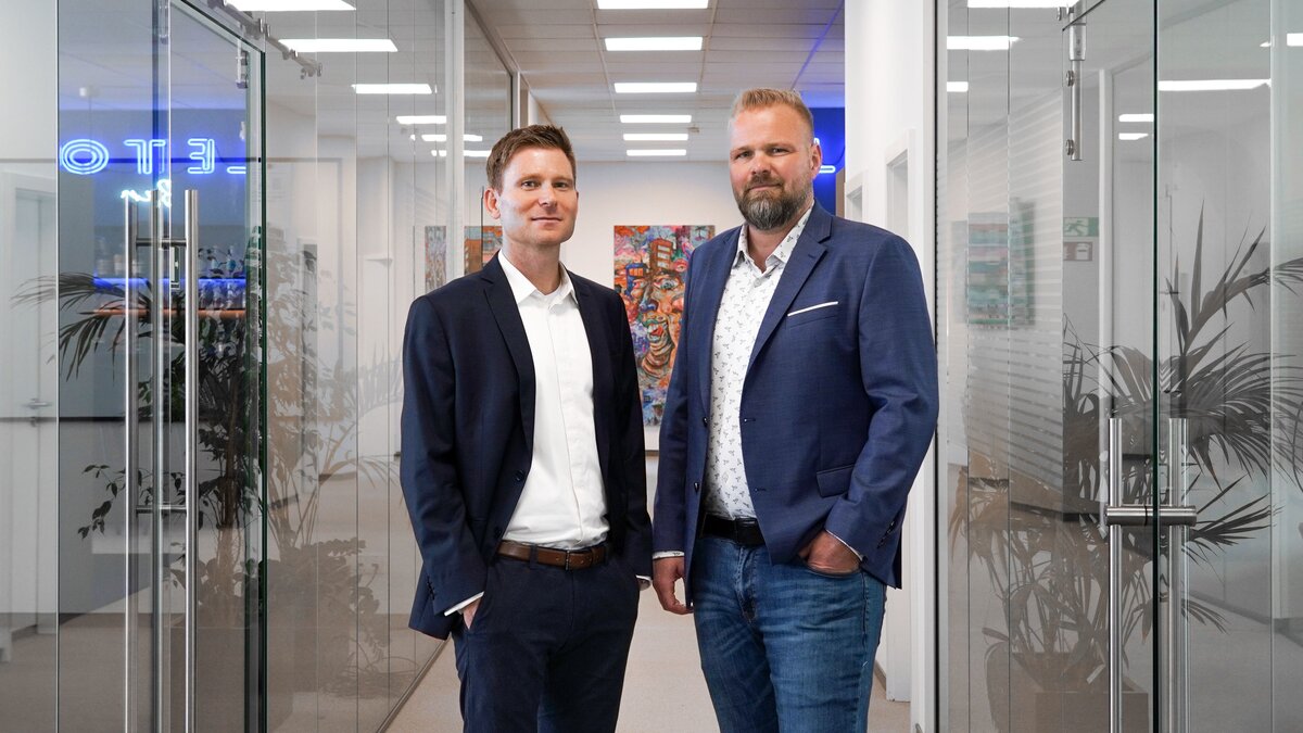 Die Geschäftsführer von Leiton stehen in einem modernen Büro und schauen souverän in die Kamera. 