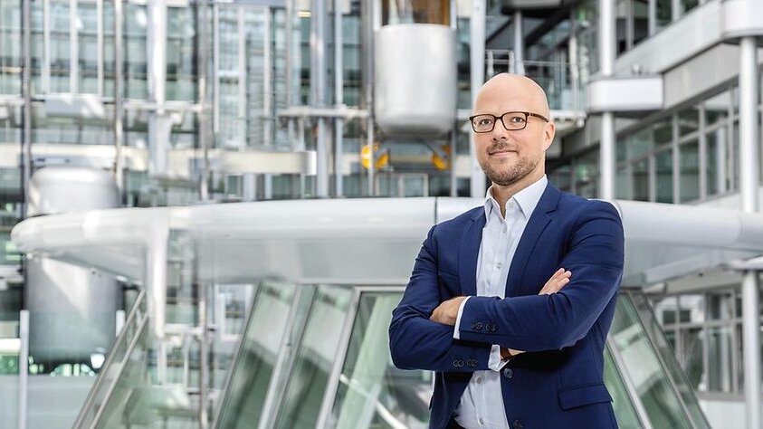 Zu sehen ist ein Mann im Anzug. Er steht im Atrium eines futuristischen Bauwerks. Es handelt sich um Sebastian Stietzel, Präsident der IHK Berlin.