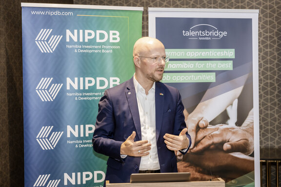 Sebastian Stietzel, Präsident der IHK Berlin, steht an einem Redepult. Links und rechts befinden sich Roll‑up‑Banner mit den Logos von NIPDB und Talentsbridge Namibia