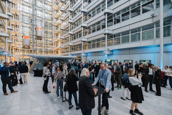 Zu sehen ist ein futuristischer Innenhof eines großen Gebäudes, in dem sich viele Menschen aufhalten. Es handelt sich um das Kant-Atrium des Ludwig Erhard Hauses der IHK Berlin.