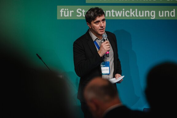 Ein Mann spricht auf einer Bühne vor Publikum.