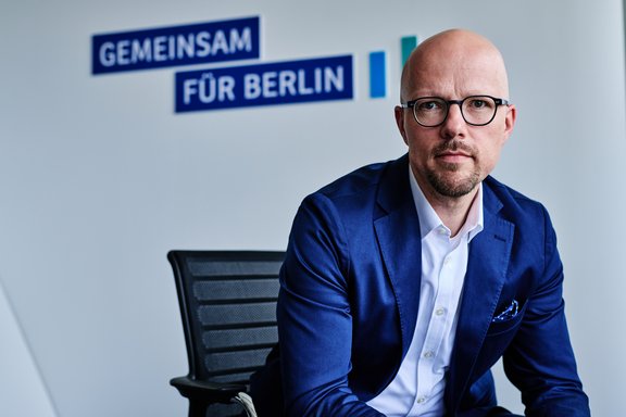 IHK-Präsident Sebastian Stietzel sitzt vor einer blauen Rückwand mit dem Schriftzug Gemeinsam für Berlin 