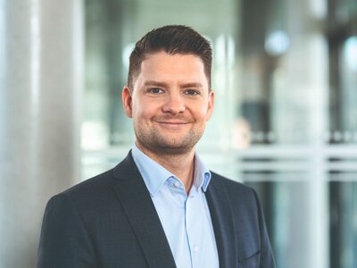Zu sehen ist ein mittelalter Mann im Sakko mit kurzen braunen Haaren.