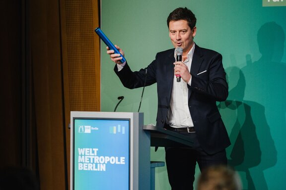 Ein Mann spricht auf einer Bühne in ein Mikrofon.