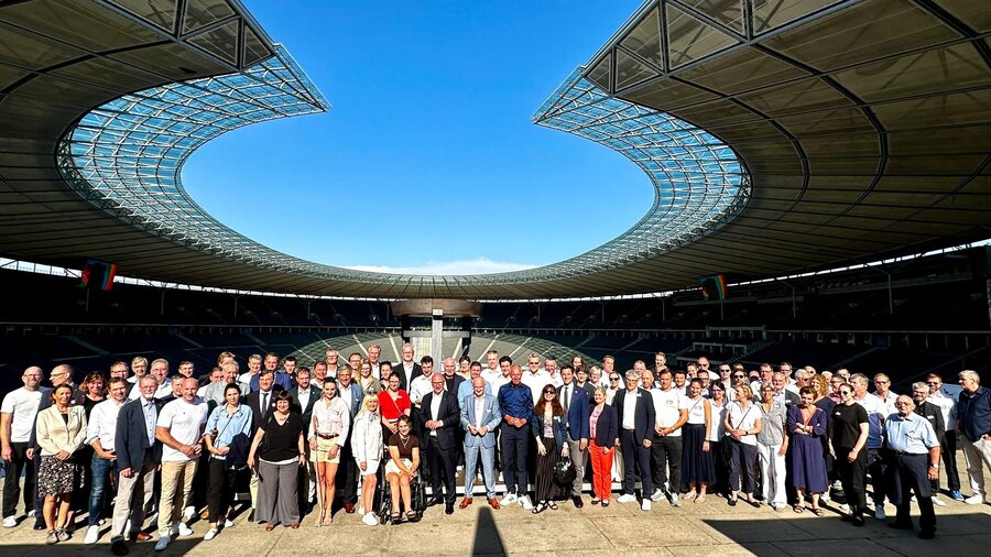 Zu sehen ist eine große Gruppe an Menschen die in einem Stadion stehen. Es handelt sich um das Olympiastadion Berlin.