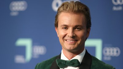 Mann mit grünem Samt-Sakko und Fliege lächelt vor blauem Hintergrund mit Audi-Logos