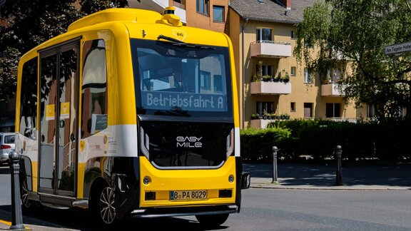 Ein autonomer Bus der Berliner Verkehrsbetriebe steht an einer Straße mit Wohnhäusern im Hintergrund