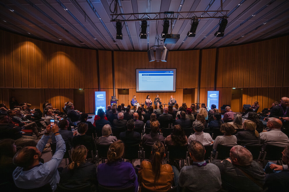 Blick in den Veranstaltungsraum des Jakobb‑Kongresses mit Publikum und Bühne.