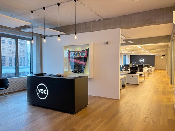 Empfangstresen mit beleuchtetem YOC-Logo im Bürogebäude der YOC AG in Berlin, moderner Arbeitsplatz mit Schreibtischen und Computern im Hintergrund