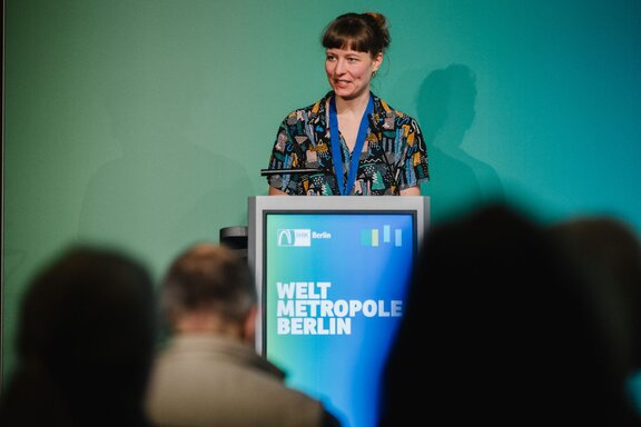 Eine Frau hält eine Rede am Pult vor Publikum.