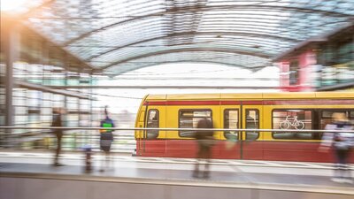 Zu sehen ist eine einfahrende S-Bahn in einen Bahnhof mit Glasdecke. Es handelt sich um den Hauptbahnhof Berlin. Das Bild ist durch lange Belichtungszeit verschwommen.