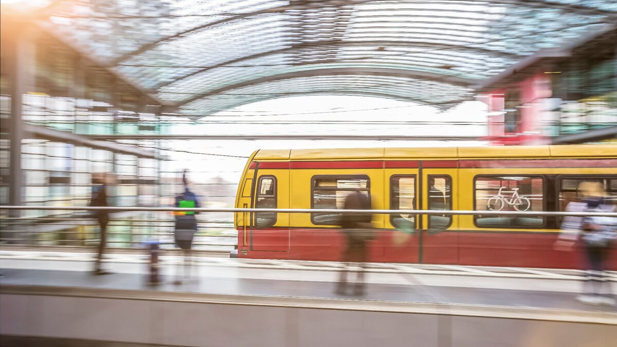 Zu sehen ist eine einfahrende S-Bahn in einen Bahnhof mit Glasdecke. Es handelt sich um den Hauptbahnhof Berlin. Das Bild ist durch lange Belichtungszeit verschwommen.