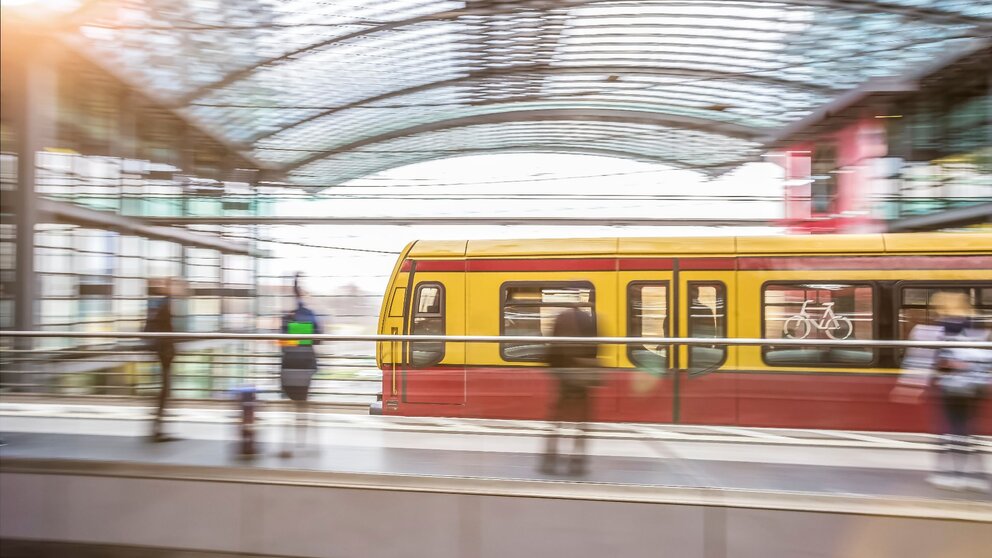 Zu sehen ist eine einfahrende S-Bahn in einen Bahnhof mit Glasdecke. Es handelt sich um den Hauptbahnhof Berlin. Das Bild ist durch lange Belichtungszeit verschwommen.