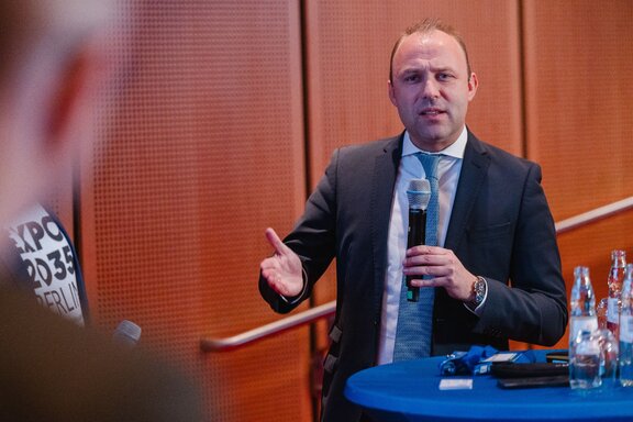 Ein Mann redet an einem Stehtisch Mit Mikrofon.