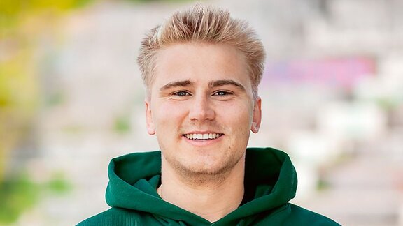 Ein junger Mann mit blonden Haaren lächelt in die Kamera. 