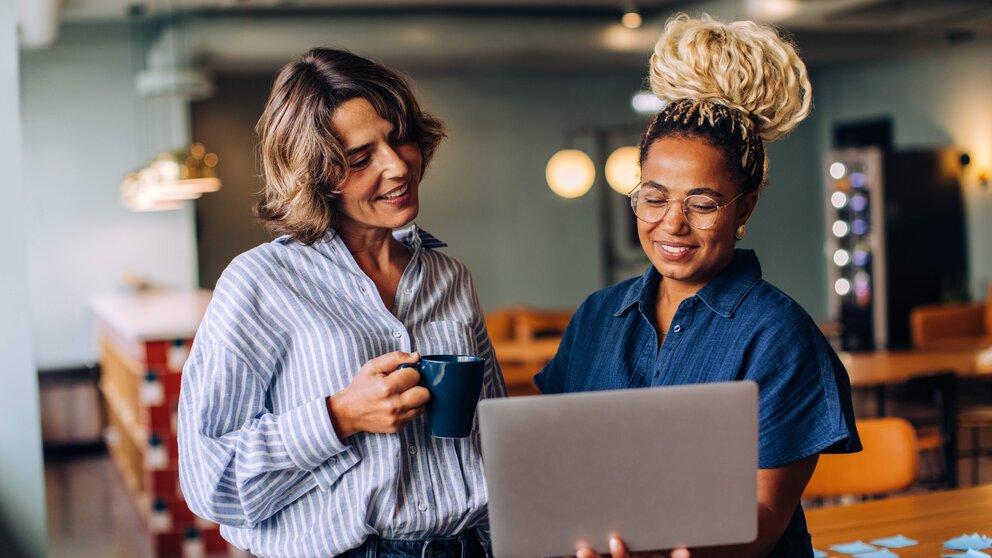Symbolbild mit zwei Frauen in einer Gesprächssituation, eine hält einen Laptop in der Hand
