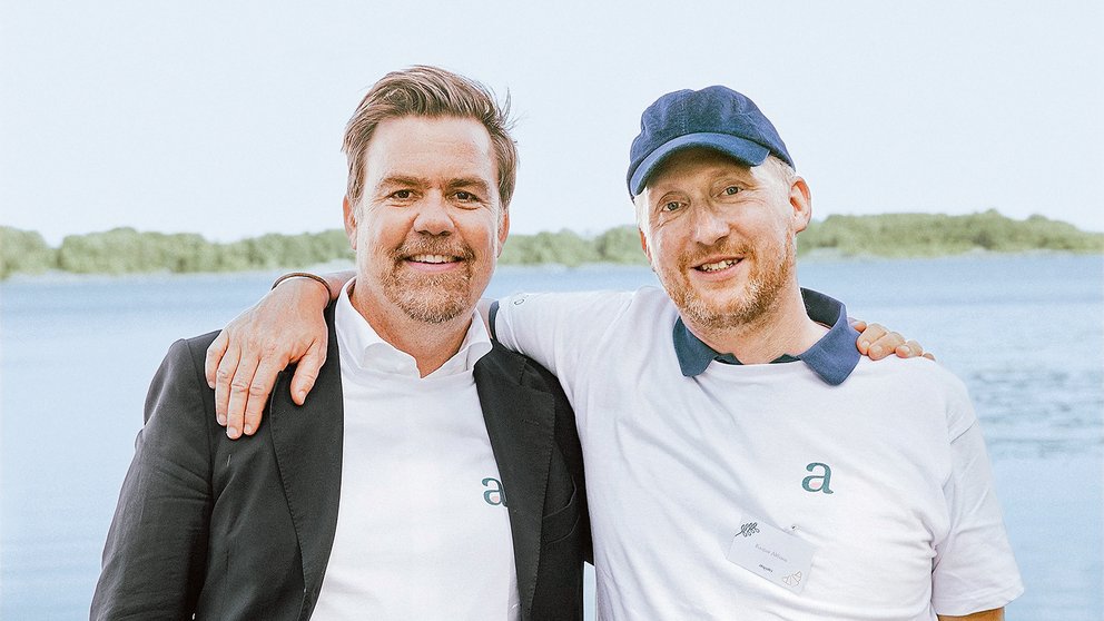 Auf dem Bild sind zwei weiße Männer im mittleren Alter zu sehen. Der Mann links trägt ein weißes Hemd und ein dunkles Jacket, der Mann rechts ein Basecap und ein weißes Polo-Shirt mit blauem Kragen.