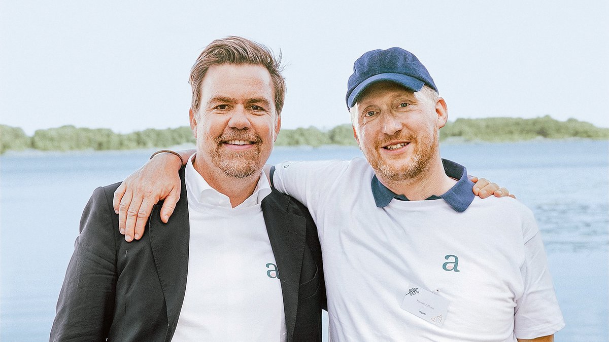 Auf dem Bild sind zwei weiße Männer im mittleren Alter zu sehen. Der Mann links trägt ein weißes Hemd und ein dunkles Jacket, der Mann rechts ein Basecap und ein weißes Polo-Shirt mit blauem Kragen.
