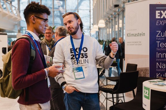 Ein Mann der EXPO 2035 spricht mit einem Interessierten auf einem Kongress der IHK.