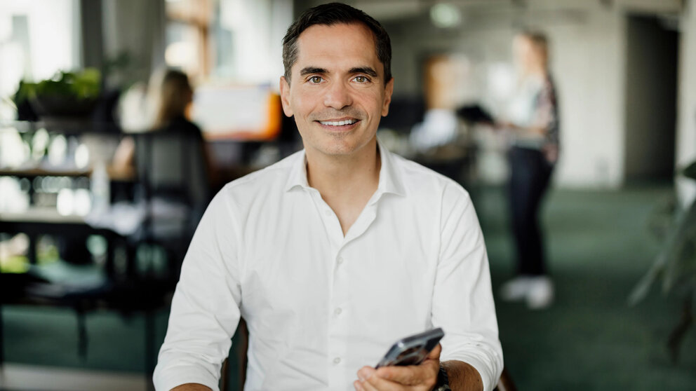 Zu sehen ist ein mittelalter Mann im Büro, der freundlich-lächelnd ein Handy in der Hand hält – es ist der CEO von Taxfix, Martin Ott