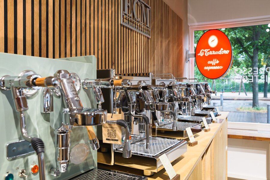 Auf dem Bild sind viele Espressomaschinen zu sehen, die aufgereiht vor einer Wand stehen.