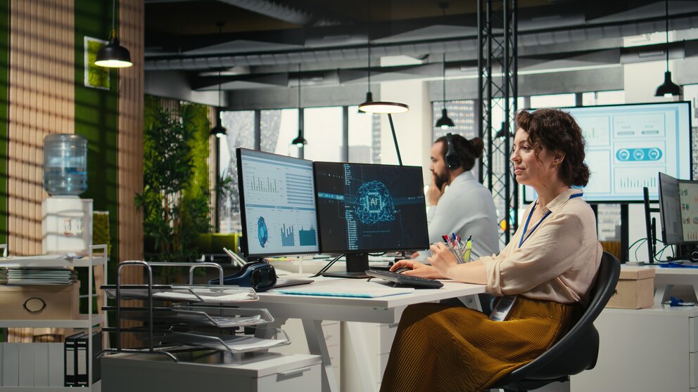 Eine Frau sitzt in einem Büro am Schreibtisch und arbeitet mit KI