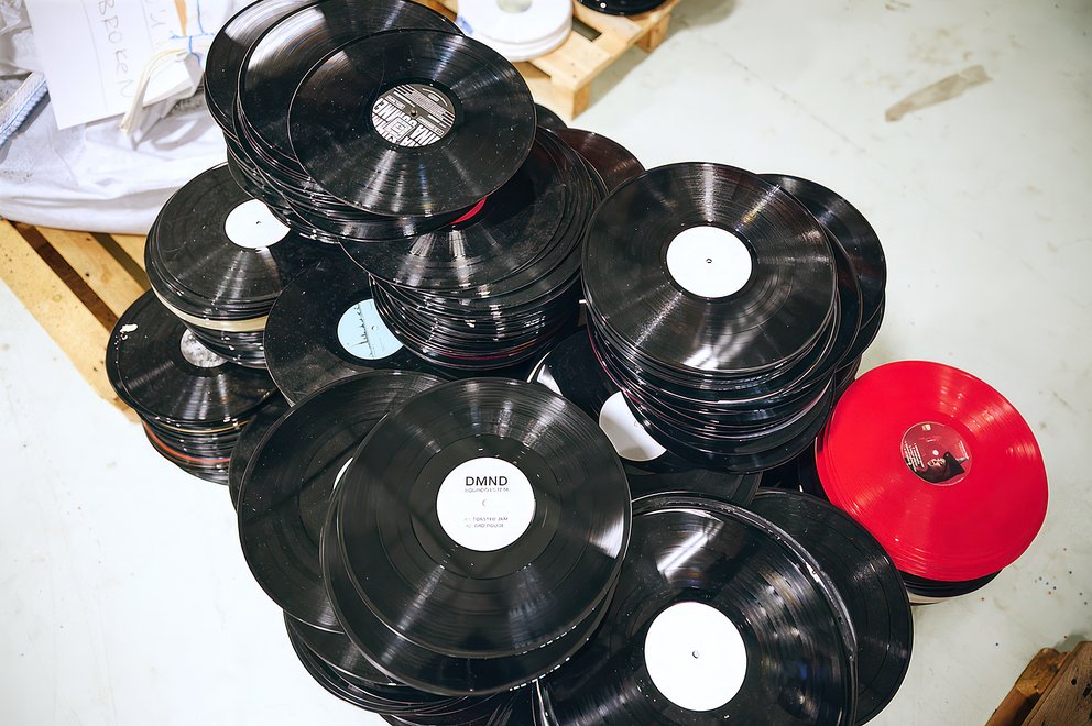 Mehrere Stapel schwarzer Schallplatten und eine rote Schallplatte auf hellem Boden