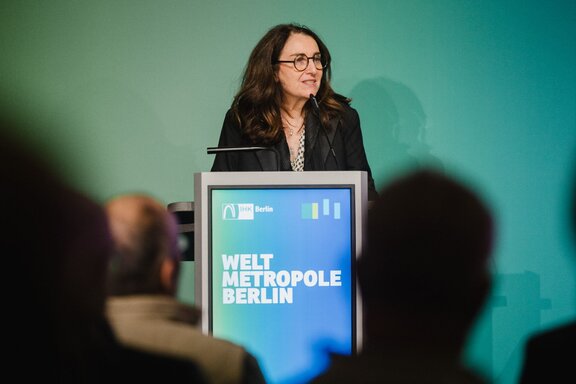 Eine Frau steht am Redepult auf einer Bühne vor Publikum.