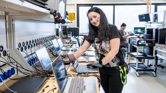 Eine junge Frau arbeitet an einem Laptop und lächelt in die Kamera. 
