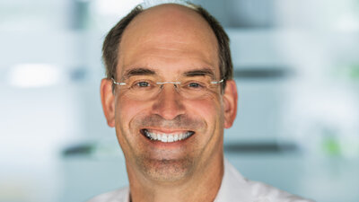 Ein mittelalter lachender Mann mit Brille und weißem Oberhemd vor einem hellen, unscharfen Hintergrund. Es ist der Geschäftsführer des Elektrogroßhandels Obeta.