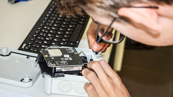 Ein Schüler arbeitet mit einem Schraubendreher an einer Feinstaubmessstation.