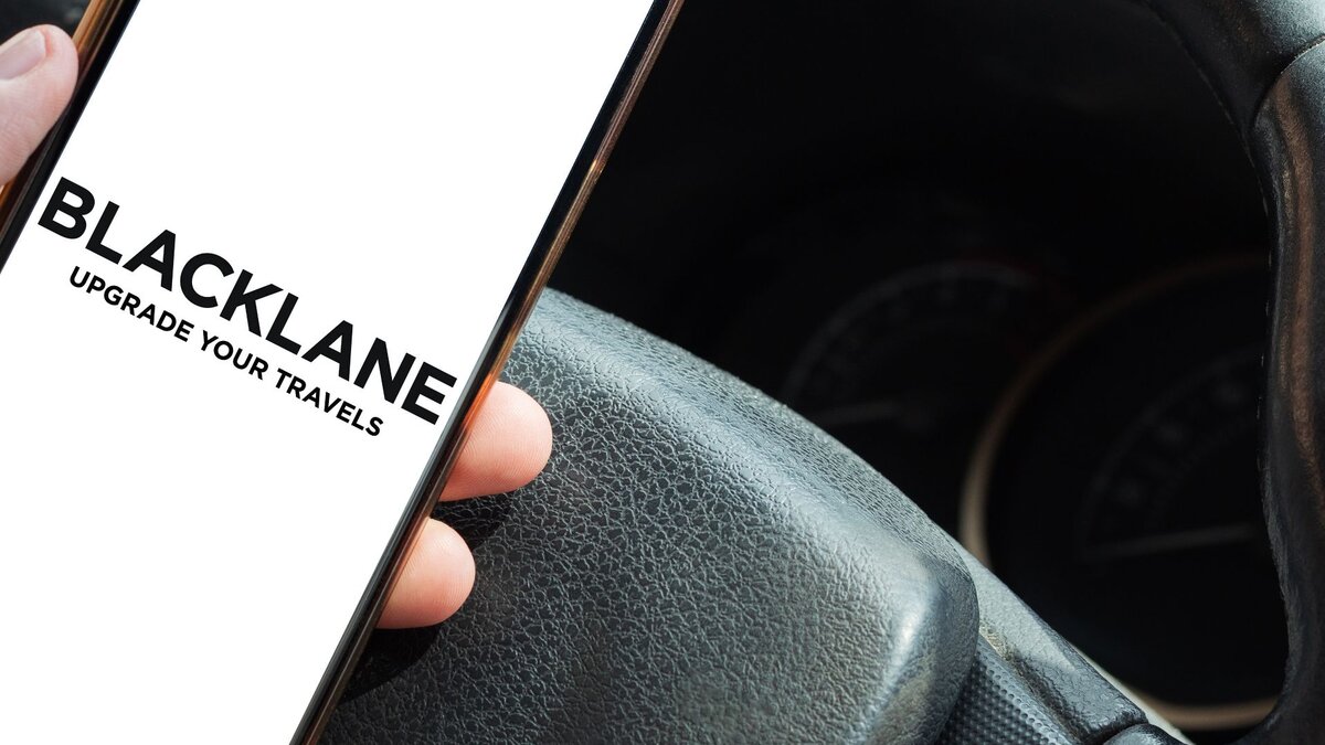 Zu sehen ist ein Smartphone in der Hand einer Person. Die Hand liegt auf einem Autolenkrad. Auf dem Smartphone steht "Blacklane". Dabei handelt es sich um den Berliner Chauffeurdienstleister.