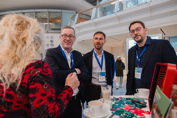 Eine mit dem Rücken zugewandte Frau unterhält sich mit drei Männern an einem Stehtisch im Ludwig Erhardt Haus.