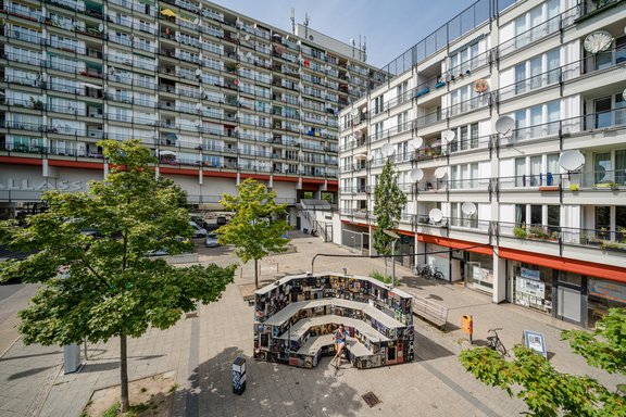 Innenhof eines Wohnkomplexes mit mehrstöckigen Gebäuden, Bäumen und einer runden Bücherwand im Zentrum