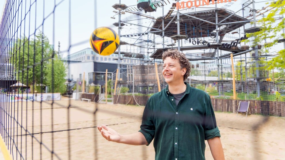 Ein Mann mittleren Alters steht am Netz eines Beachvolleyballfeldes.