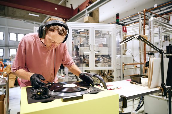 Mann mit Kopfhörern und schwarzen Handschuhen bedient Plattenspieler in industrieller Werkstatt