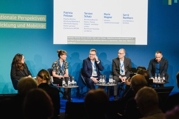 Blick auf eine Bühne mit vier sitzenden, sich unterhaltenden Speakern.