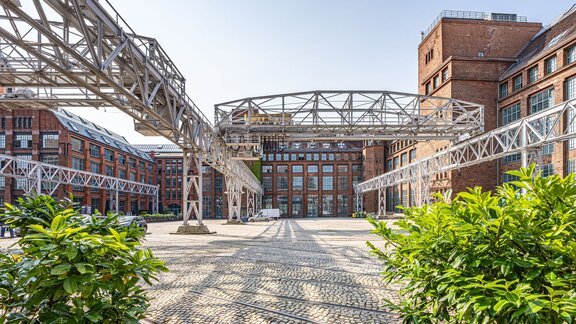 Zu sehen ist eine Gewerbehof, dessen Häuser aus rotem Backstein bestehen. Es handelt sich um den Gewerbehof Amperium am Humboldthain in Berlin mitte.