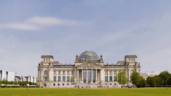 Der Reichstag in Berlin mit seiner markanten Glaskuppel und umliegenden Grünflächen unter blauem Himmel
