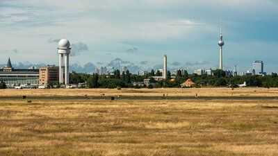 zu sehen ist eine weite Wiese, im Hintergrund der Fernsehturm von Berlin. Es handelt sich um das Tempelhofer Feld.
