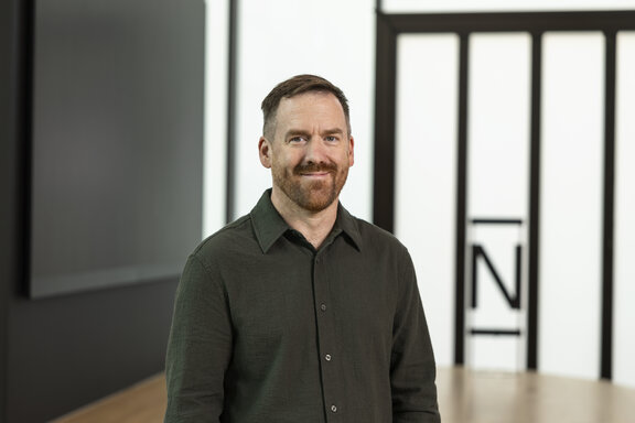 Ein Mann mit kurzen Haaren und einem dunklen Hemd lächelt in die Kamera. Es ist Dan Hardaker von N26.