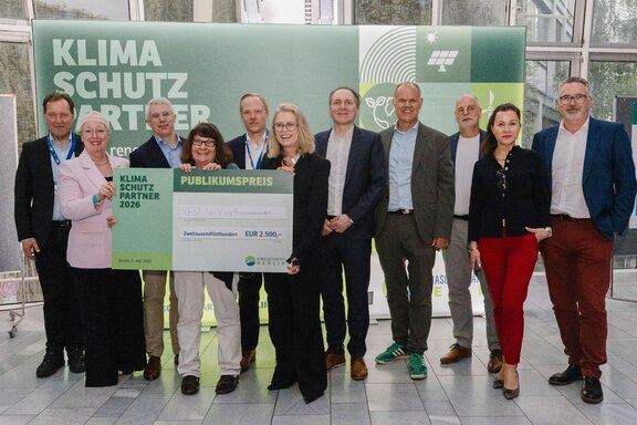 Zu sehen sind mehrere Personen, die vor einer Fotowand stehen und freundlich in die Kamera schauen.